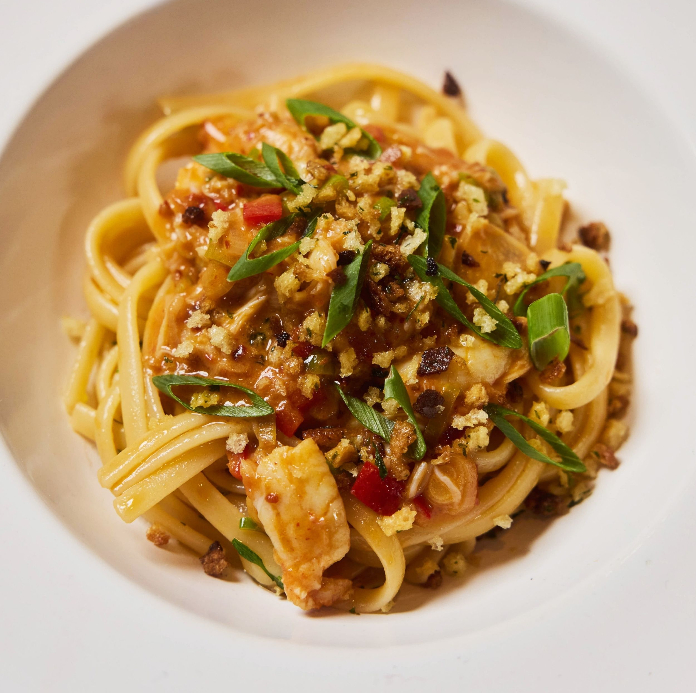 A plate of spaghetti topped with crab, chopped green onions, red pepper, and crispy browned crumbs in a rich red sauce.