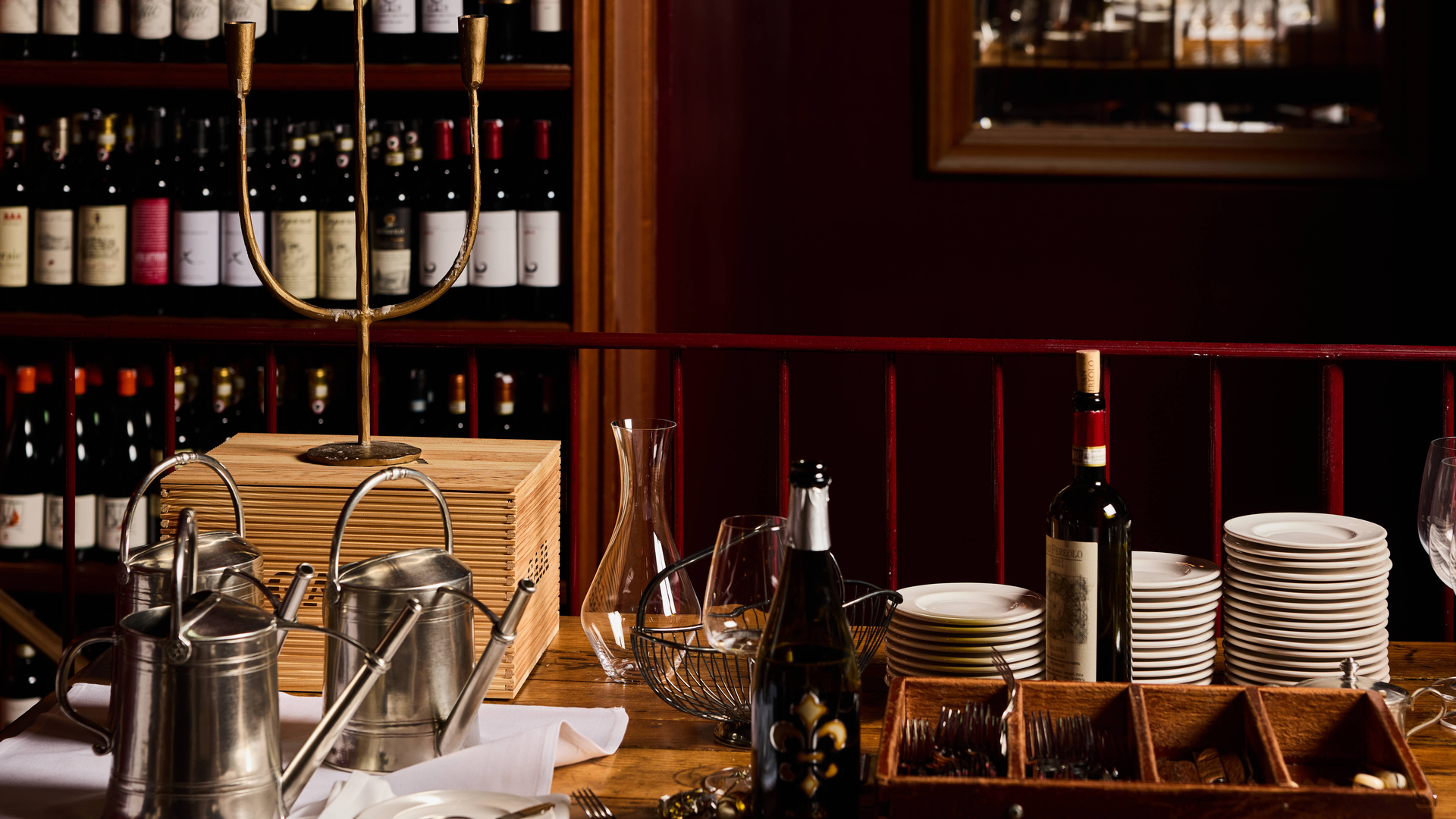A wine merchant setup with bottles of wine, plates, glasses, and metal carafes and buckets.
